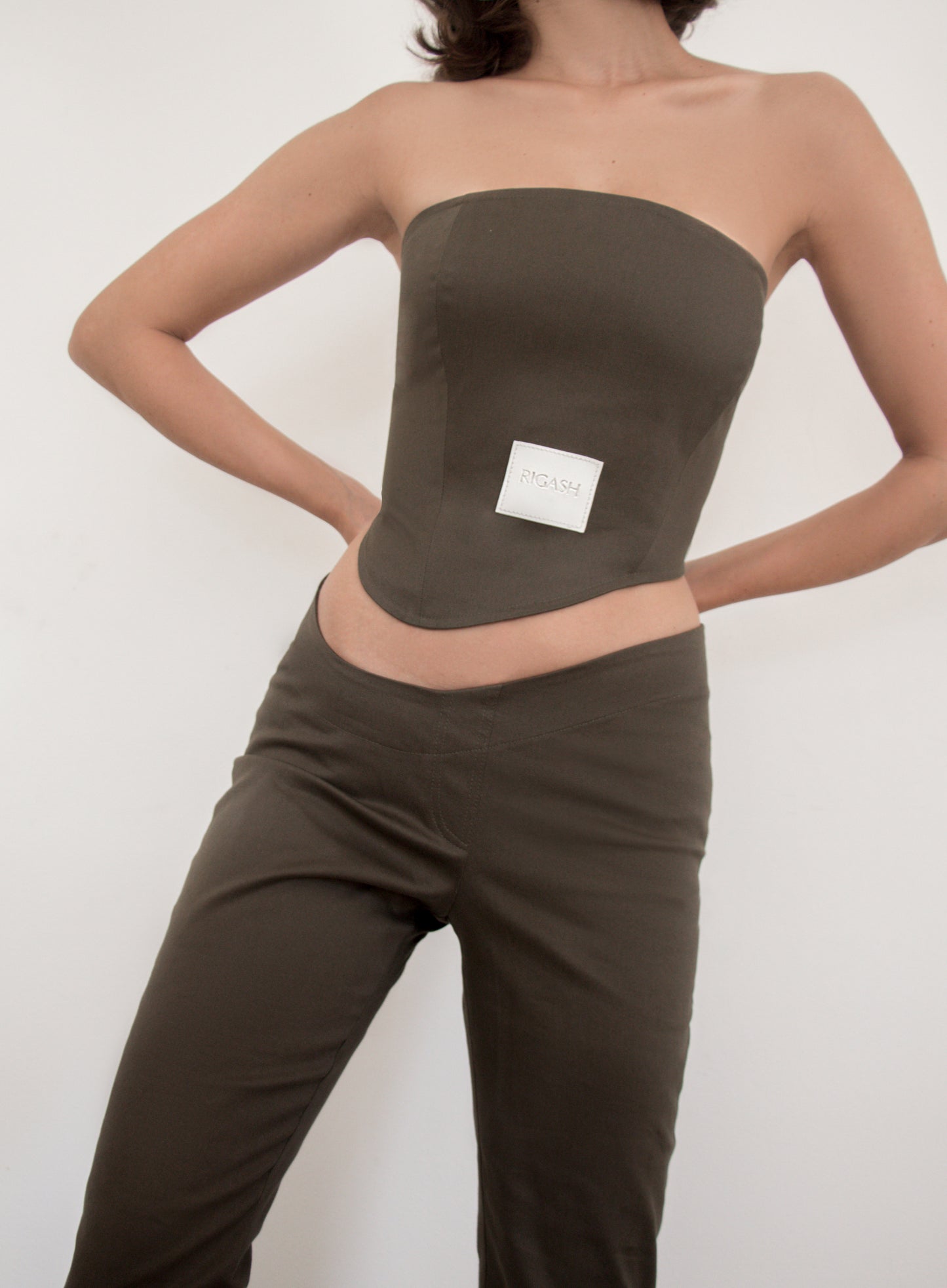 Asymmetrical low waist kick-flare trousers in olive green cotton gabardine. Inseam slit with zip fastening.